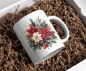 Preview: Weihnachtstasse mit festlichem Design aus Stechpalme, Weihnachtsstern und winterlichen Zweigen, liegend in einer Geschenkbox mit Füllmaterial. Perfektes Geschenk für die Weihnachtszeit.